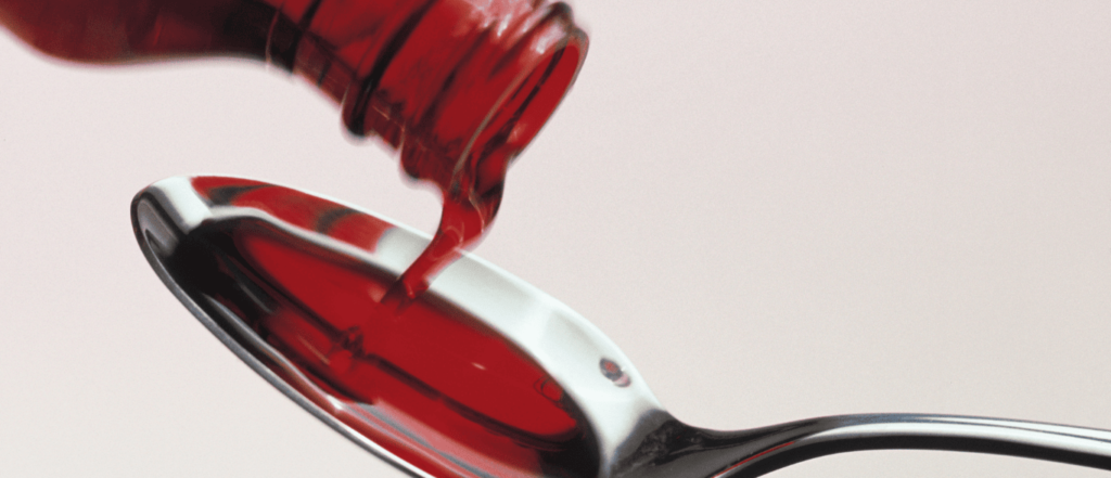 Frasco de jarabe echando del líquido en una cuchara